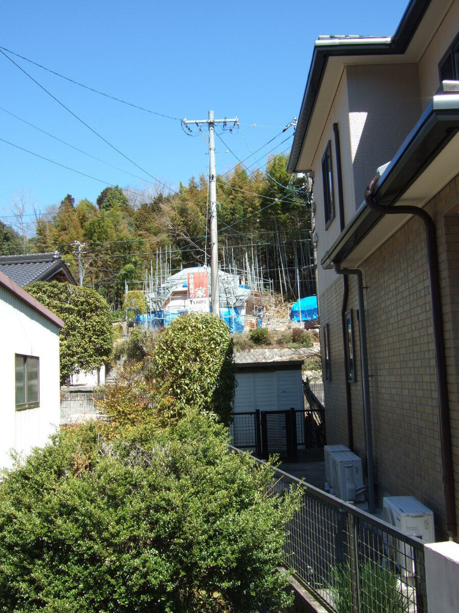 A geodesic dome is under construction up a hill in the distance, viewed through the gap between two houses.