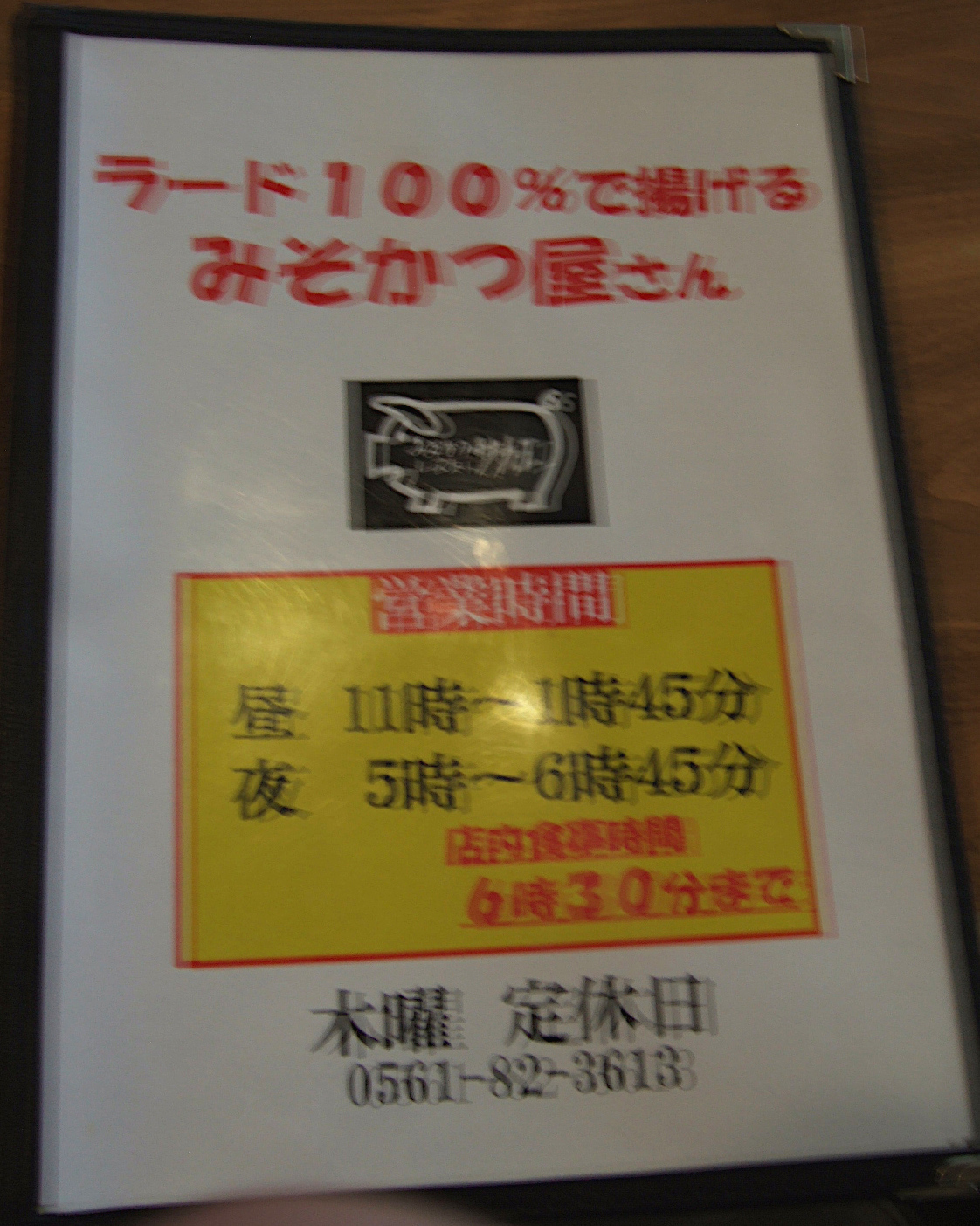 A blurry photograph of the cover of a restaurant menu reading (in English translation) “Restaurant for Miso Cutlet Deep-fried in 100% Lard” and listing opening days and times with the phone number of the shop