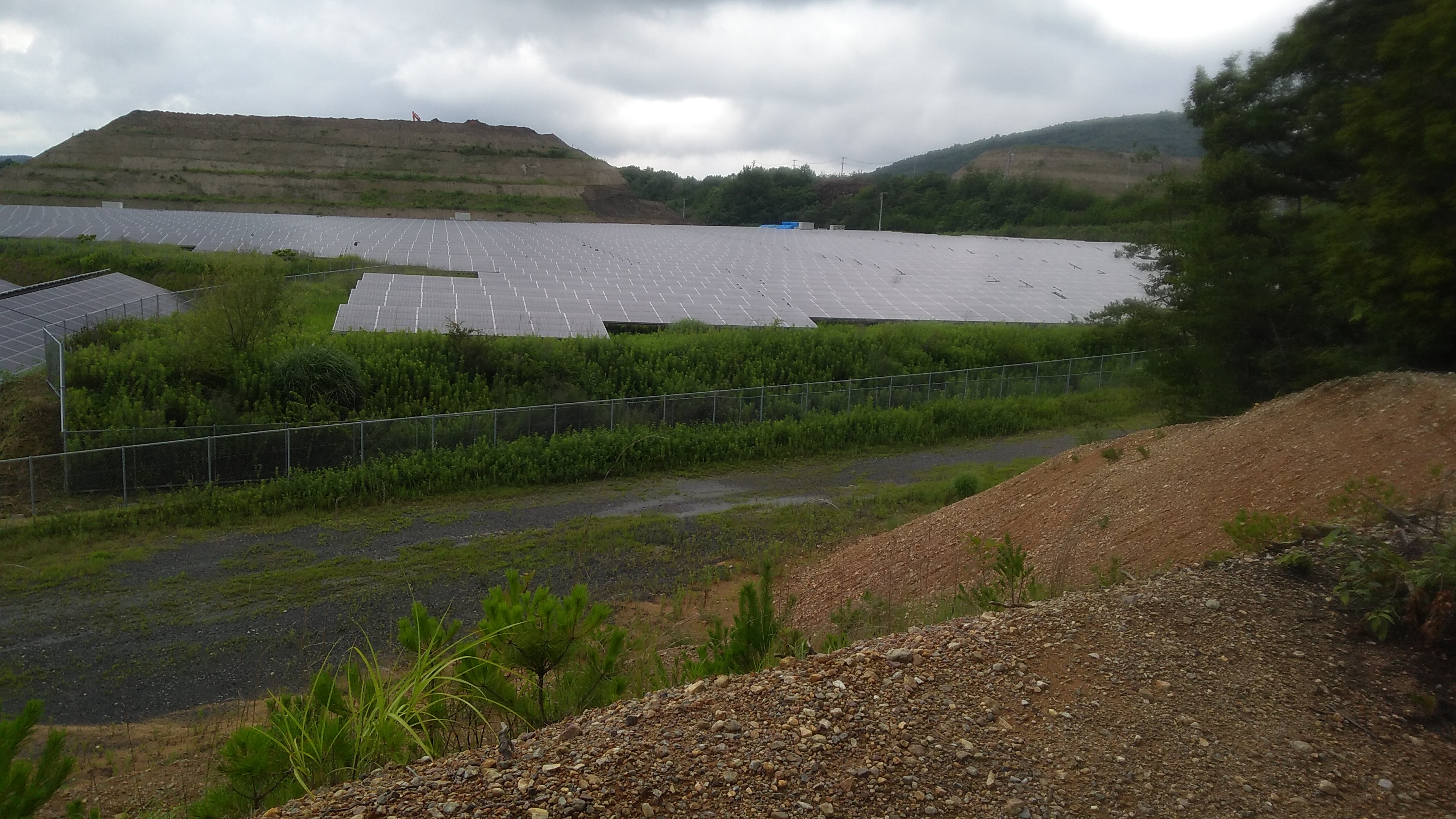 Massive expanse of solar panels in a mountain valley, with the exposed soil of a ridge terraced by earthmoving equipment visible on the horizon