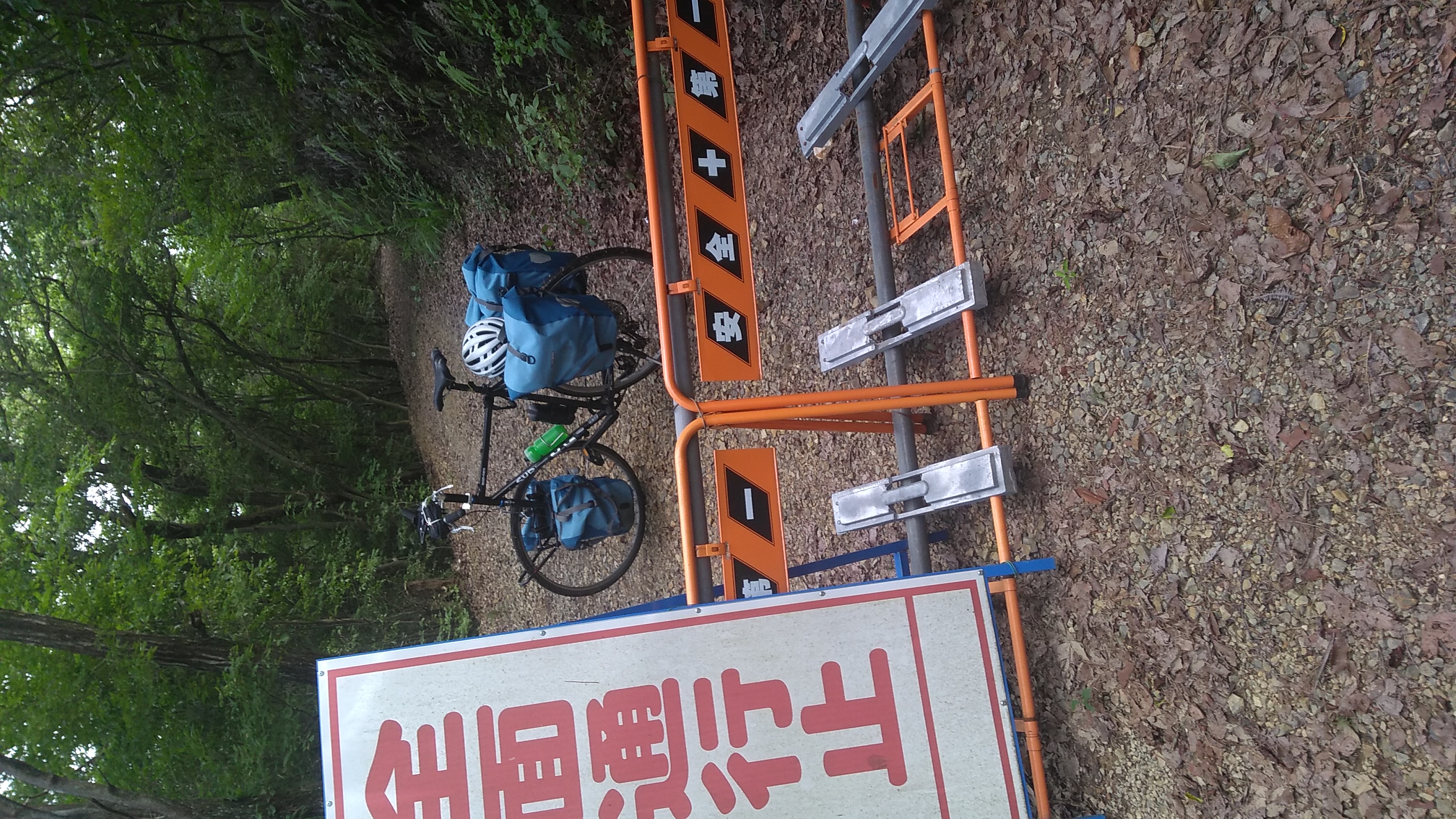 A bicycle with front an rear panniers parked beyond a sign reading (in English translation) “Road not passable to any traffic.”