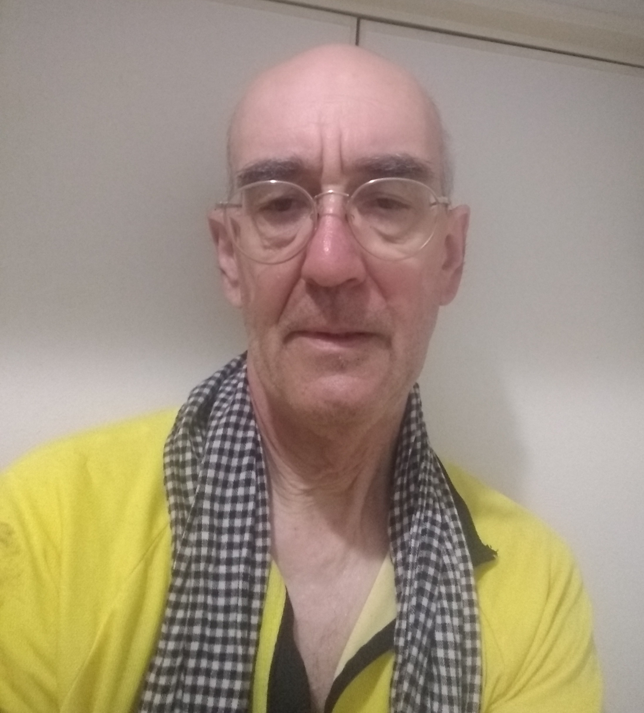 Elderly bald man in a yellow riding jersey and gold-rim glasses with a sweat-soaked cotton scarf draped over his neck gaping at the camera in a state of exhaustion.