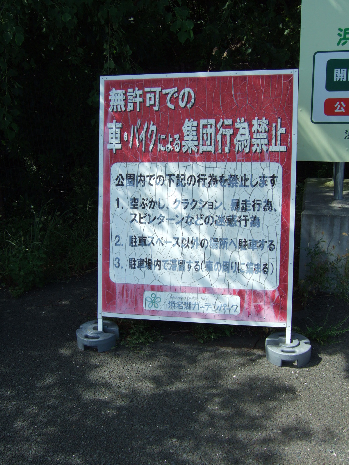 Sign in Japanese, reading (in English translation):\nUnauthorized group activities involving cars or motorcycles are prohibited!\nThe following activities are prohibited in the park grounds:\n1. Revving engines, blowing horns, reckless driving, spinning donuts, and other nuisances.\n2. Parking outside the designated parking area.\n3. Hanging out in the parking area (i.e. gathering around vehicles).