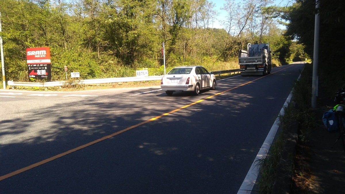 A white sedan and a truck driving past the sign at the roadside.