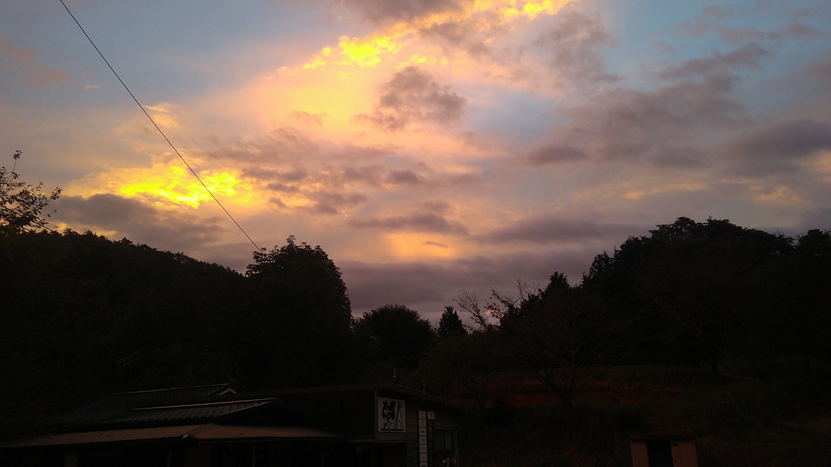 Brilliant patches of hot yellow burn through cumulus clouds over a mountain above, with pink and purple hues touching the clouds against a blue sky.