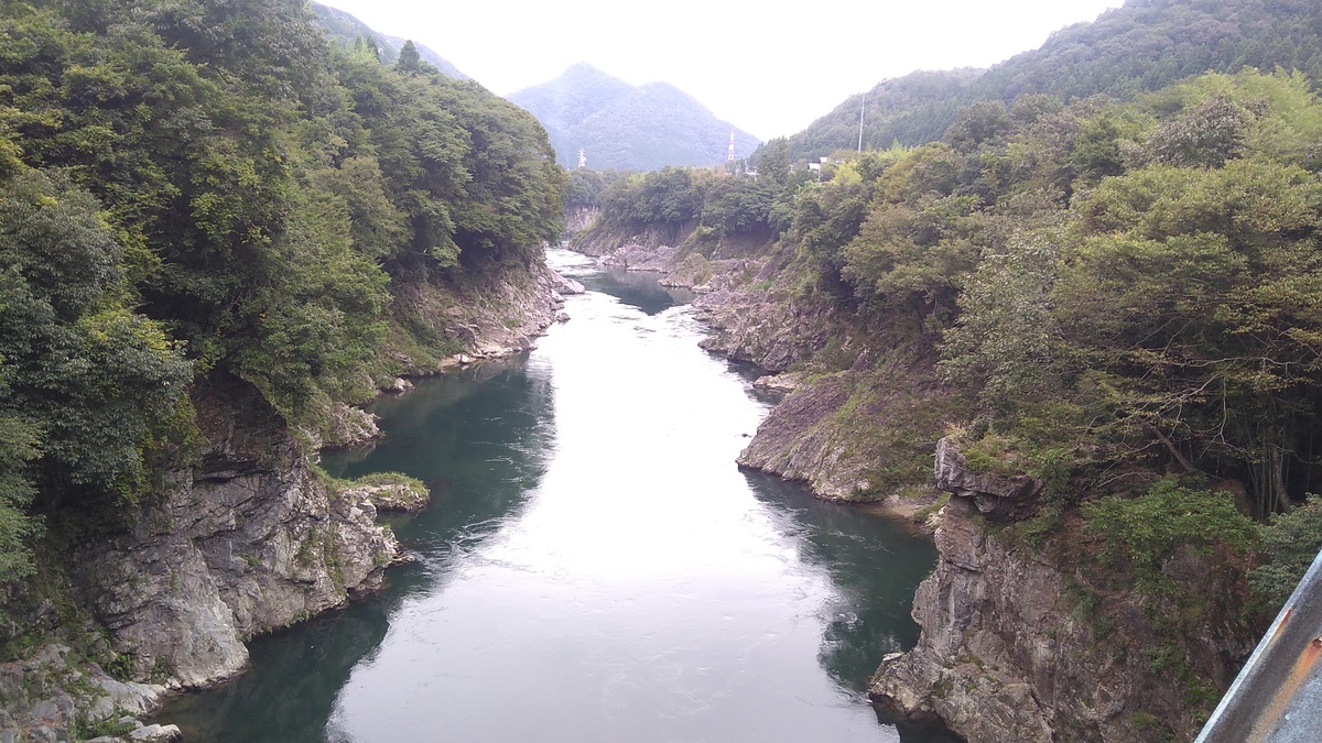 A river of crystal clear water flowing down a shallow rock-lined canyon, with dense forest encroaching on the banks at the top of the cut.