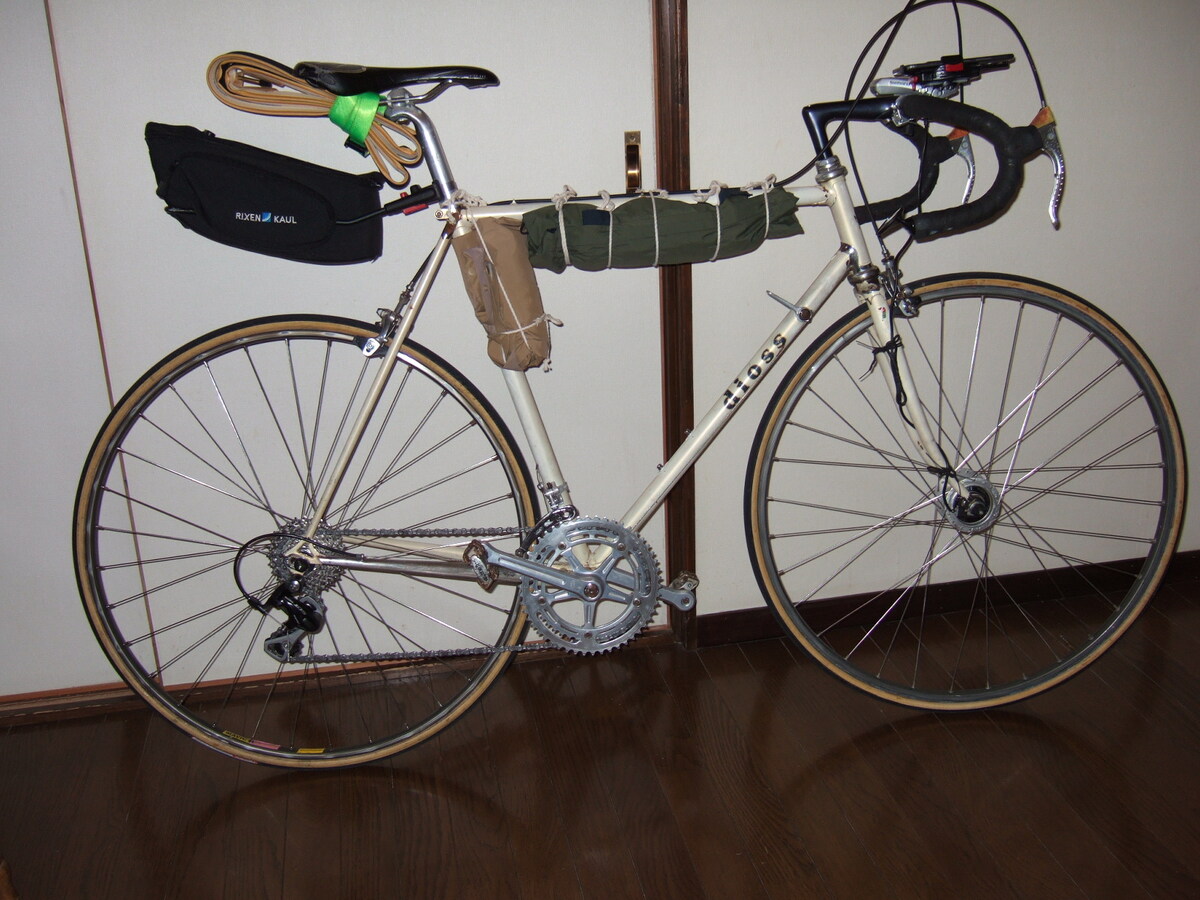 A road bike with drop handlebars, a small bag suspended to the rear off the seat post, and a couple of rolls strapped to the frame.