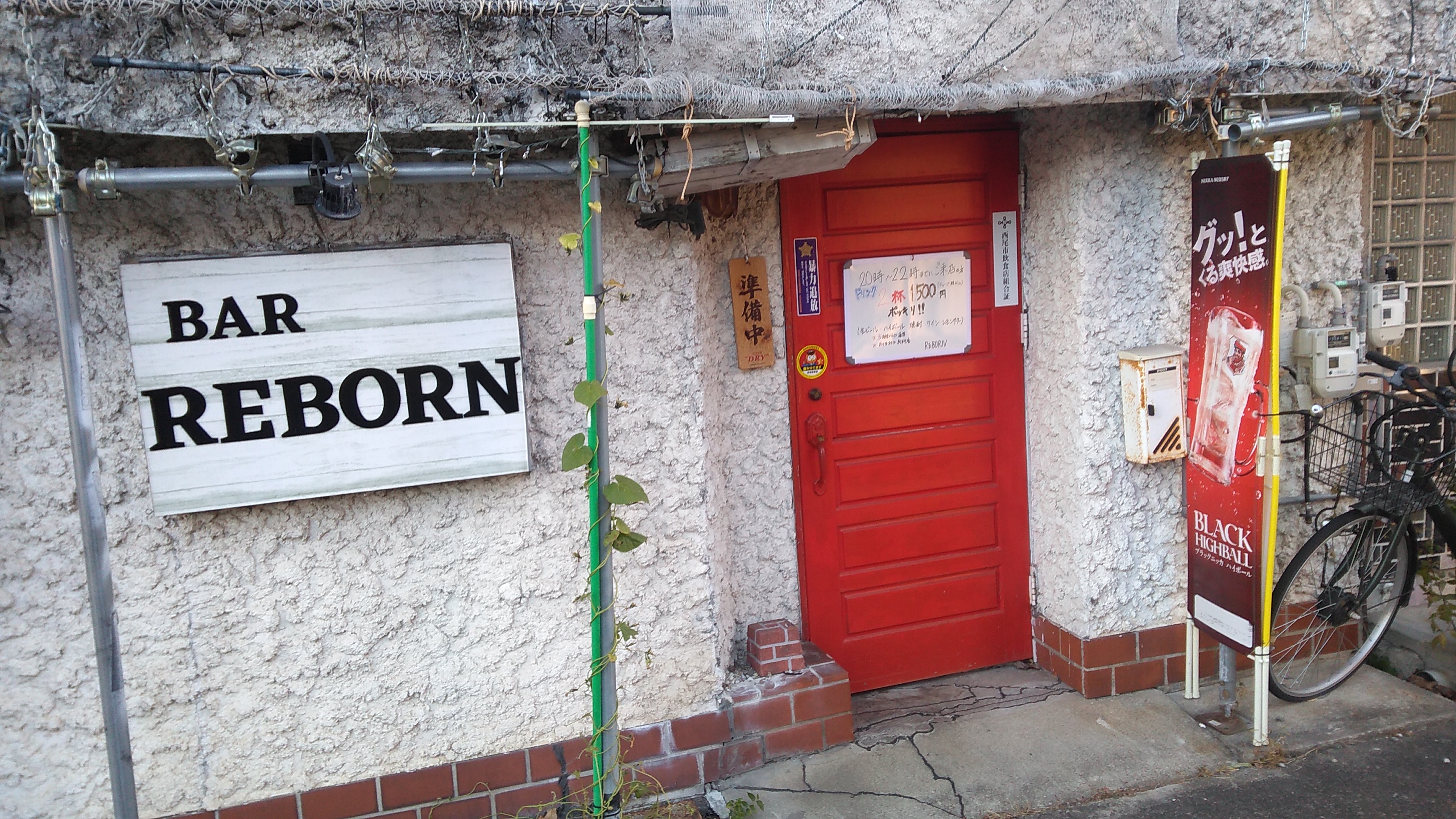 A red door with a sign reading “Bar Reborn” to the side, mounted on construction scaffolding.