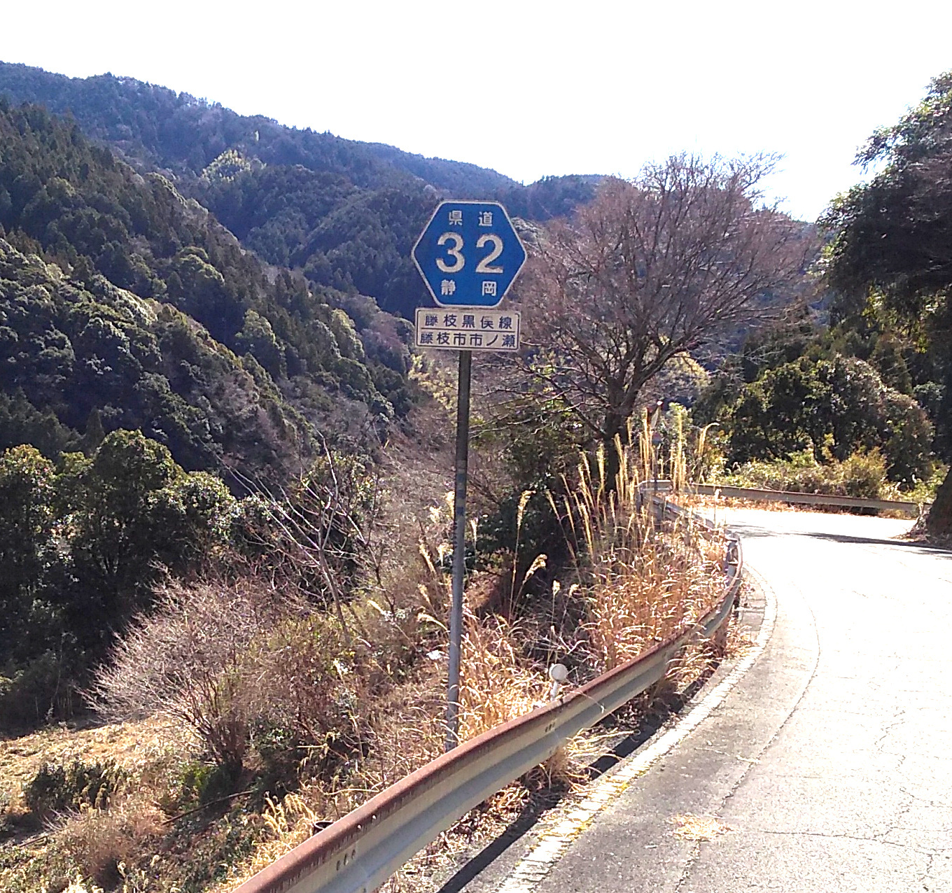 A paved mountain road with a signpost indicating it is (in English translation) “Shizuoka Prefectural Route 32” and below that “Fujieda Kuromata Right of Way / Fujieda City, Ichi-no-Se District”