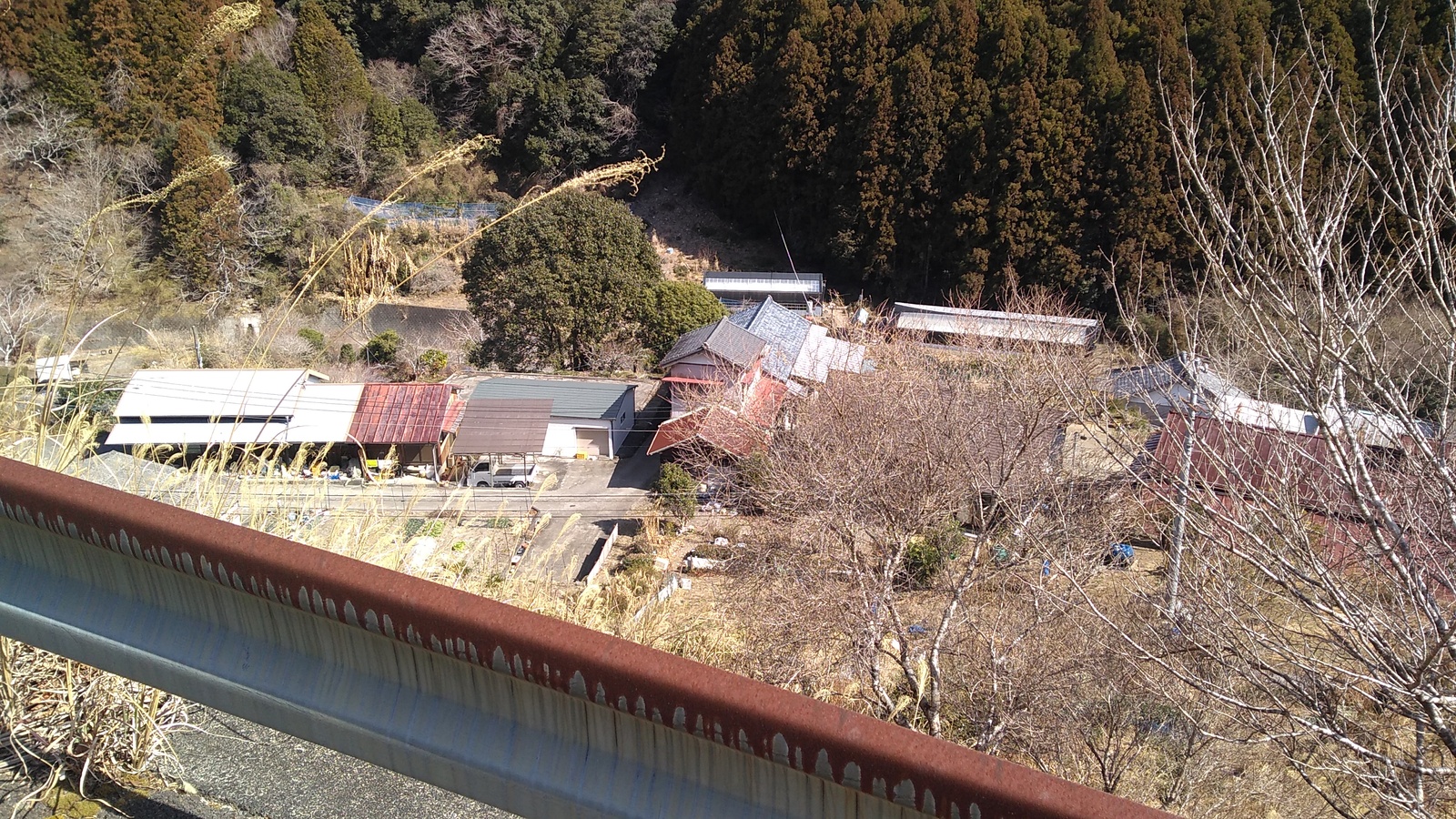 The rooftops of a small village, viewed from above, with a portion of rusted steel guardrail blocking a corner of the frame.