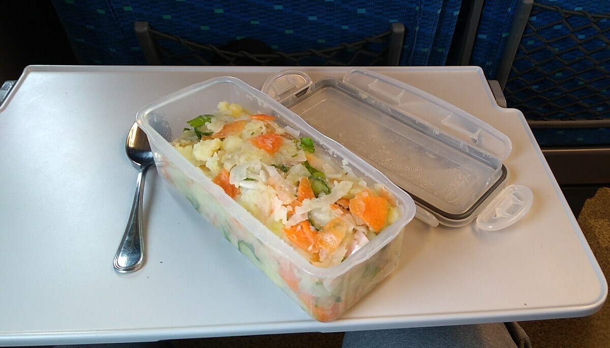 A plastic container filled with homemade potato salad, resting on a Shinkansen fold-down tray.