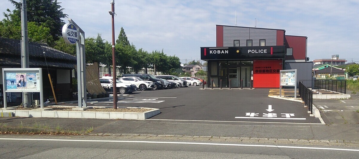 A modern red one-story building surrounded by a parking lot, with “Koban : Police” written above the door in large letters.