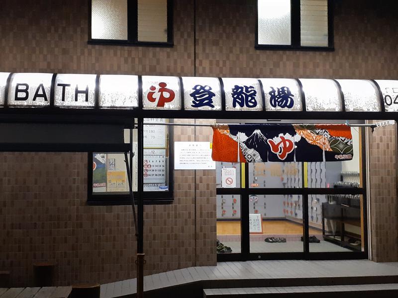 Nighttime view of the entrance to a public bath, with a noren (doorway curtain) decorated in a colorful image of Mount Fuji.