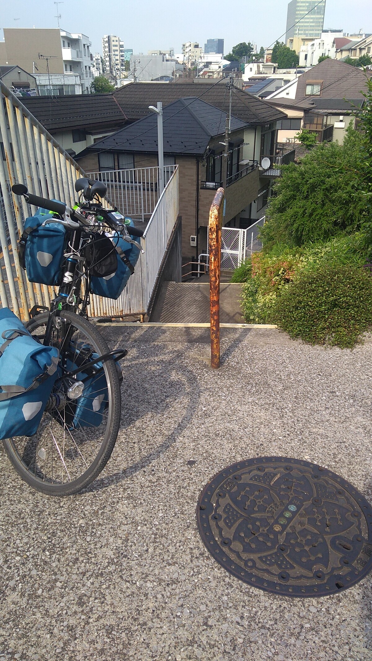 A touring bike with four panniers parked at the top of a set of concrete stairs, with a city skyline in the background.